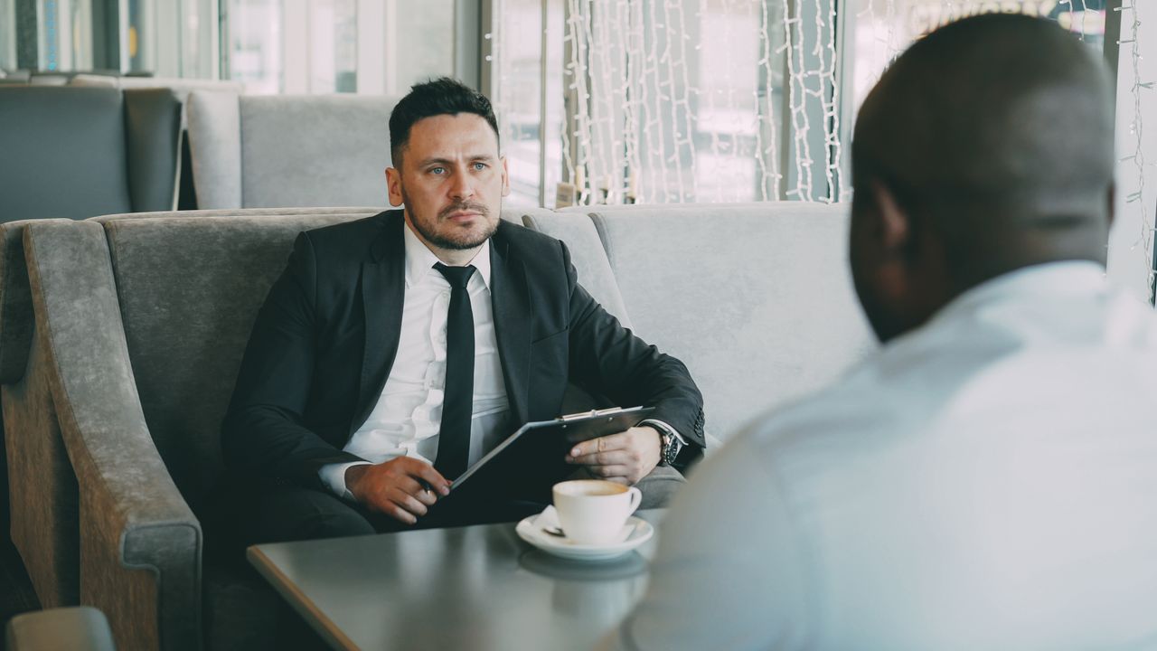 Services Two businessmen having a serious conversation over coffee in a stylish cafe setting.
